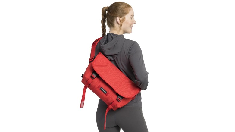 A person wearing gray sweats carrying a red messenger bag on their back