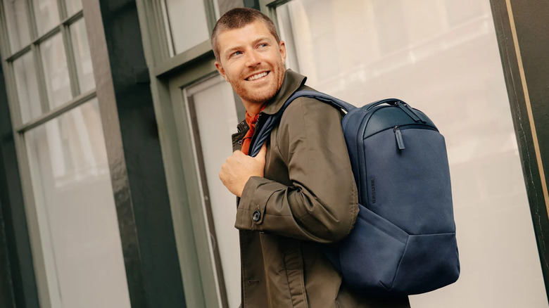 A person smiling and looking over their shoulder while wearing a navy blue backpack.
