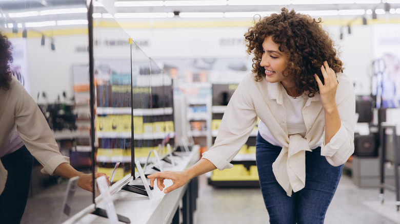 A woman looking at several TVs on display at a retail outlet.