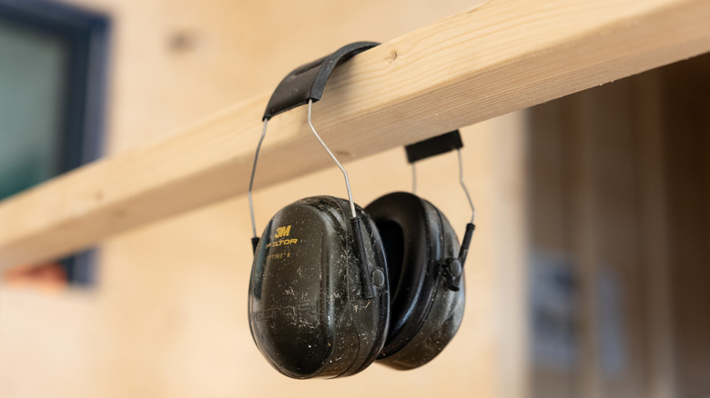 A pair of hearing protection earmuffs hanging on a wooden beam.