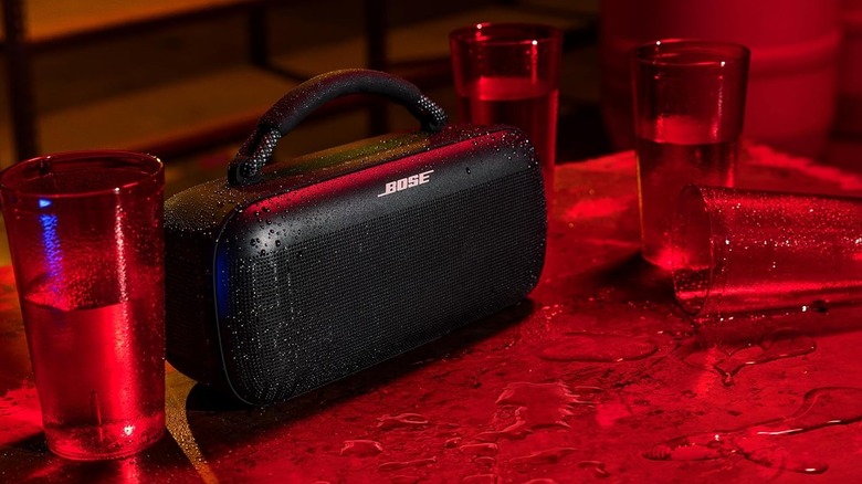The Bose SoundLink Max on a wet surface next to a spilled cup and several glasses of water.