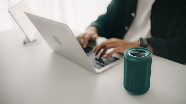 A person working on a laptop next to a tabletop Bluetooth speaker.
