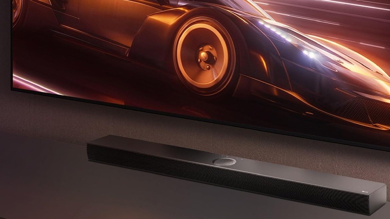 The LG S70TY placed below a wall-mounted TV on a TV stand.