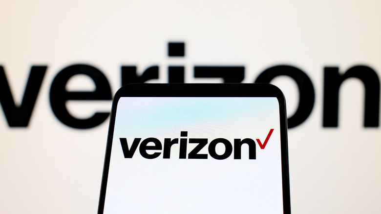 Verizon logo displayed on a smartphone screen with a blurred Verizon sign in the background.