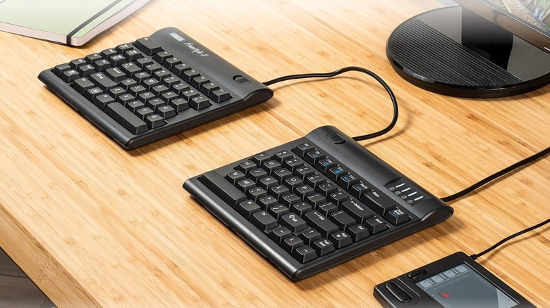 A closeup shot of the Kinesis Freestyle 2 ergonomic keyboard, the two split sides sit on a brown desk next to what looks like a drawing tablet and a notebook