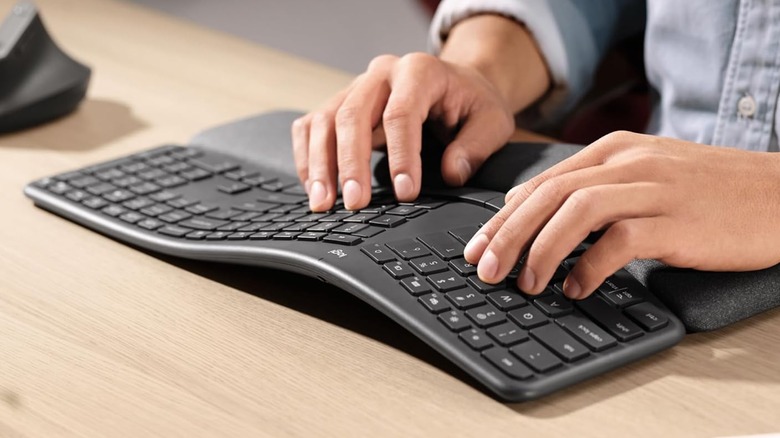A closeup of a user with both hands on a black Logitech Ergo K860 keyboard, the user is also using a black pillowed wrist pad