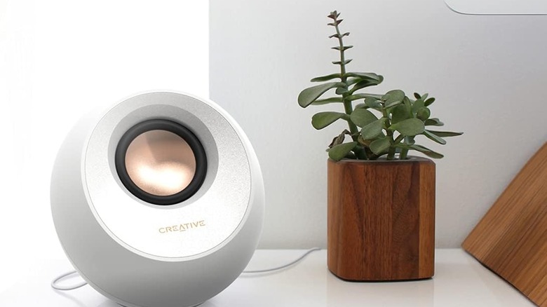 A Creative Pebble V3 speaker next to a plant.