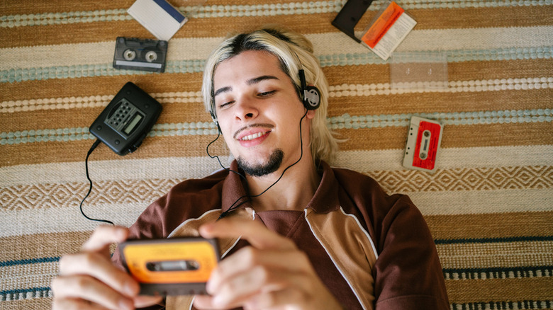 A man holding a cassette tape while listening to a Walkman