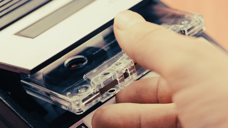 Close up of a hand putting a cassette tape in a tape player.