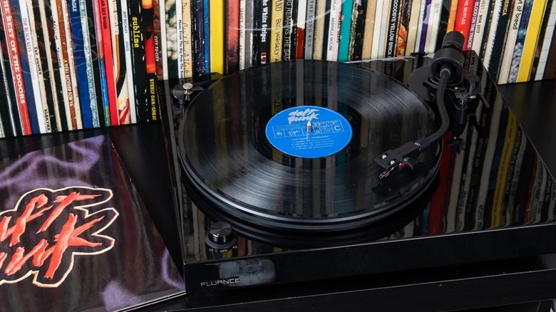 A black Fluance RT82 Reference High Fidelity Vinyl Turntable sits on top of a table next to a Daft Punk record, behind the turntable is a collection of various records