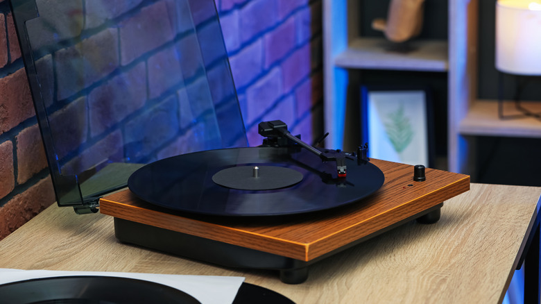 A modern looking turntable sits at the end of a desk, the device has a woodgrain footage and its tonearm is about halfway through a vinyl record