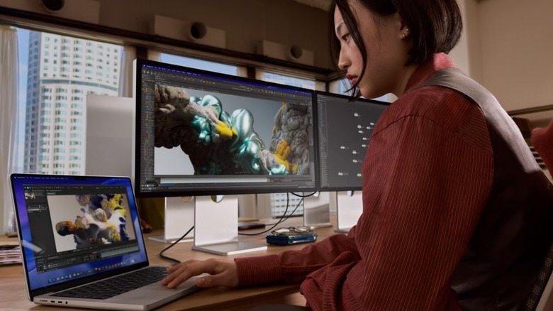 Person using a dual-monitor setup with a MacBook for creative editing work.
