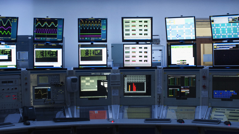 Room with multiple monitors of varying sizes displaying data and system dashboards.