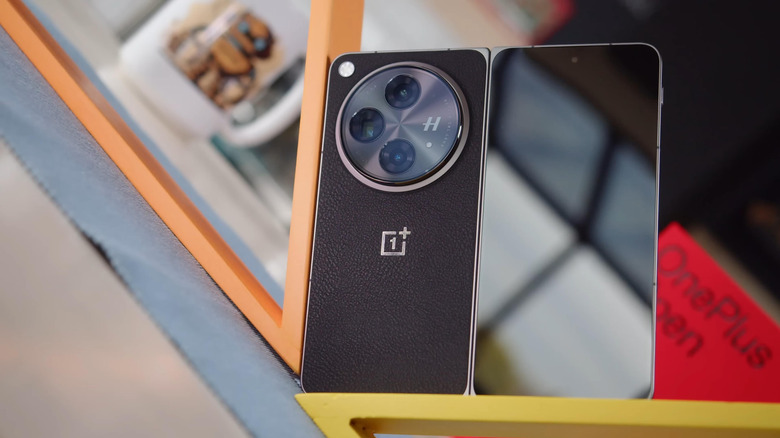 The OnePlus Open with a black leather-textured back standing on a shelf.