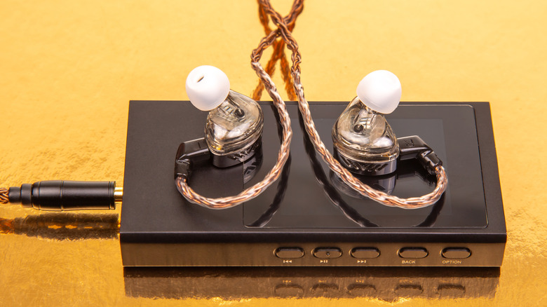 Portable DAC on yellow background with IEMs resting on top