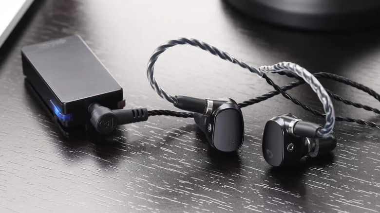 Qudelix-5K resting on dark table with IEMs plugged in