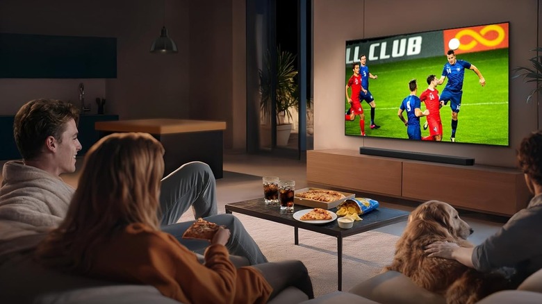 The Samsung QN80H wall-mounted in a modern living room. A family watches a football game.