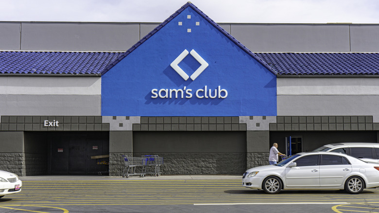 An exterior shot of a Sam's Club, including its parking lot, a person with a shopping car is visible in the photo