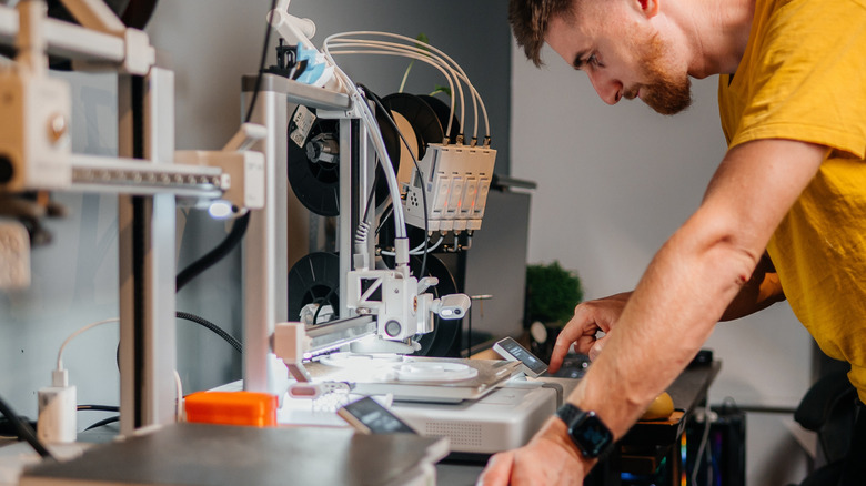 A man standing over 3D printing tools.