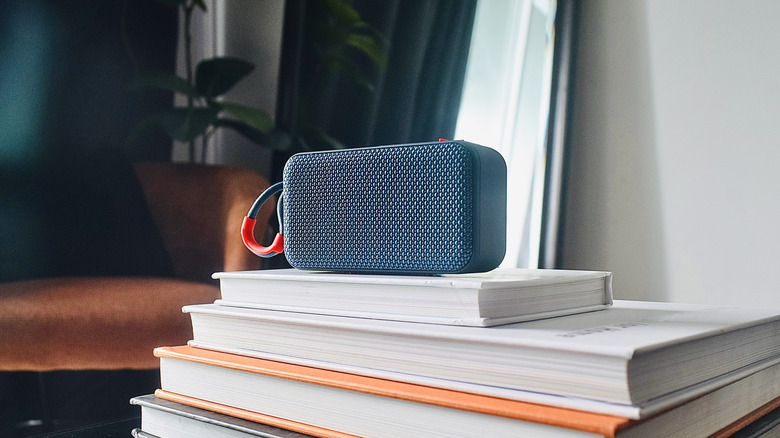 A small black wireless speaker sits a top four neatly stacked books