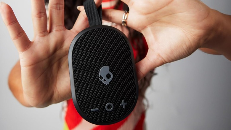 An individual holding a Skullcandy Ounce+ Wireless Bluetooth Speaker between their hands as they dramatically hold the device in front of the camera