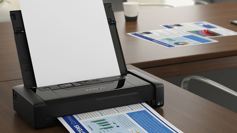 The Epson Workforce WF-110 printer on an office desk with some printed papers in the background