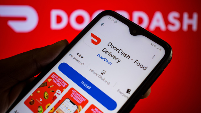 Close up of a smartphone on the store page for DoorDash, with the company logo in white on a red background behind it.