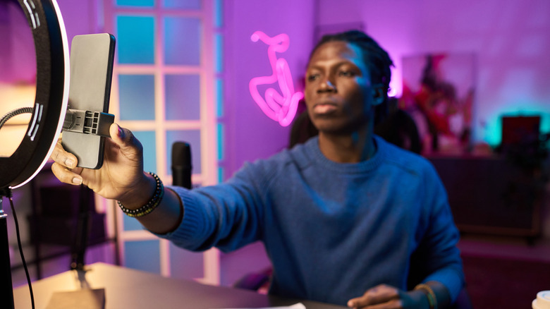 Male vlogger adjusting smartphone mounted to a ring light