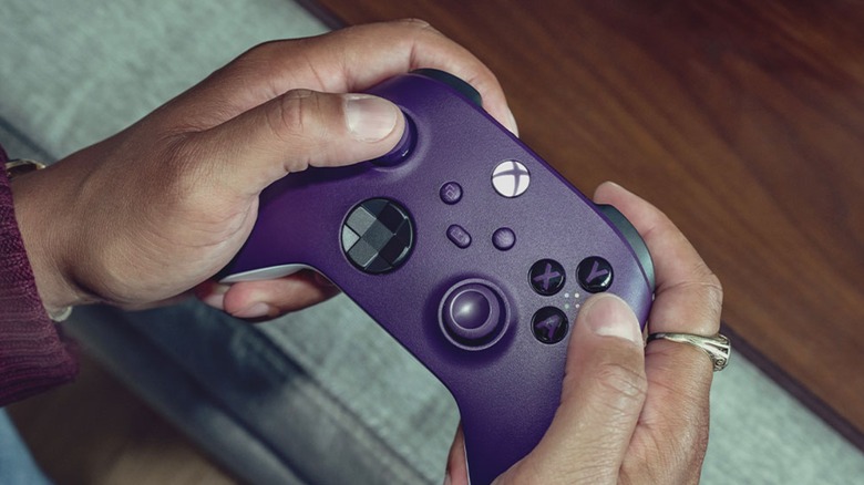 Person holding purple Xbox series X controller on sofa