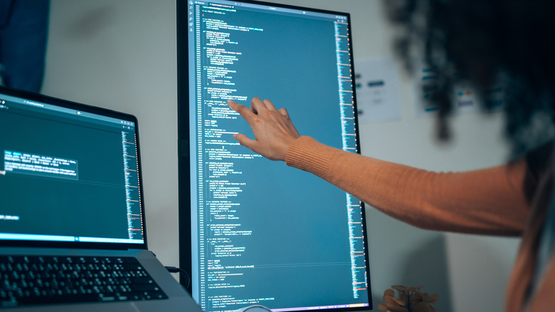 Person pointing at code on a vertical monitor in a programming workspace.