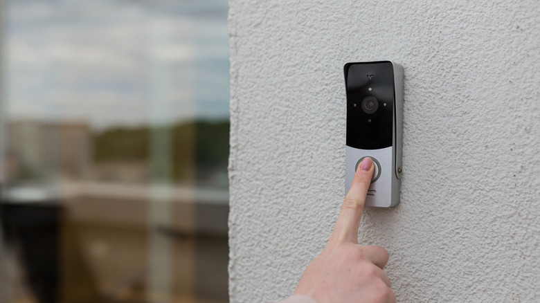A hand ringing an exterior-mounted video doorbell.