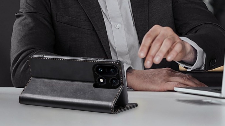 The Jasonyu Flip Wallet Case for OnePlus 15 sitting on a desk in its kickstand position, a person in a suit sits behind it