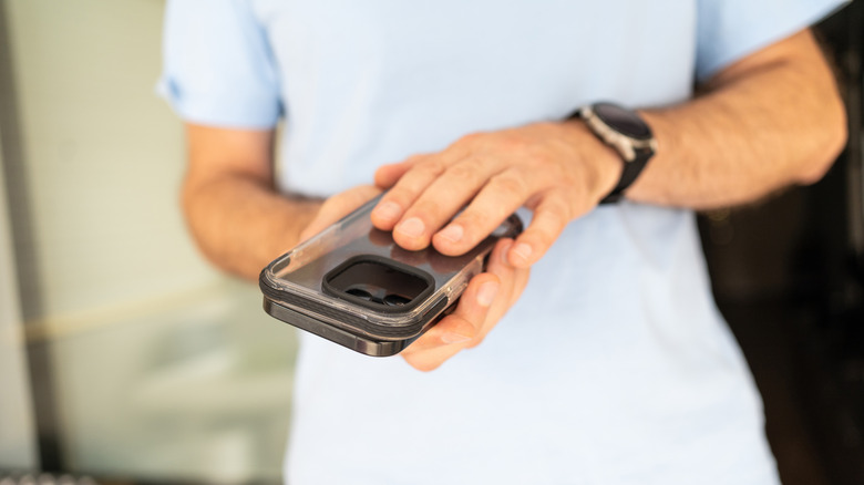 A person wearing a light blue shirt is placing a clear case on top of a smartphone