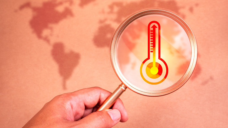 Hand holding magnifying glass focusing on temperature sensor and world map below