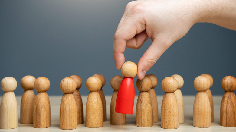 Hand picking a red wooden figure from a group of wooden figures.