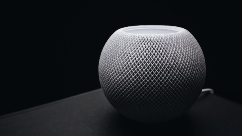 A white HomePod mini from Apple photographed in a dark light setting.