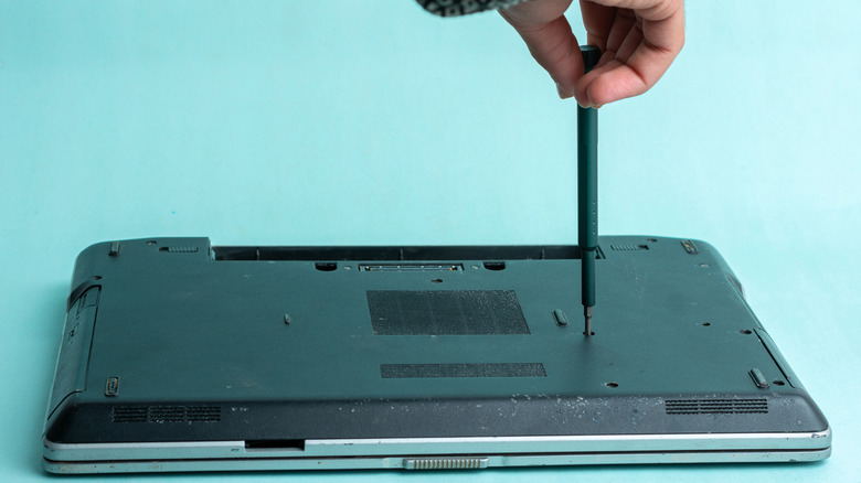 Person unscrewing the back panel of a laptop placed on a blue surface