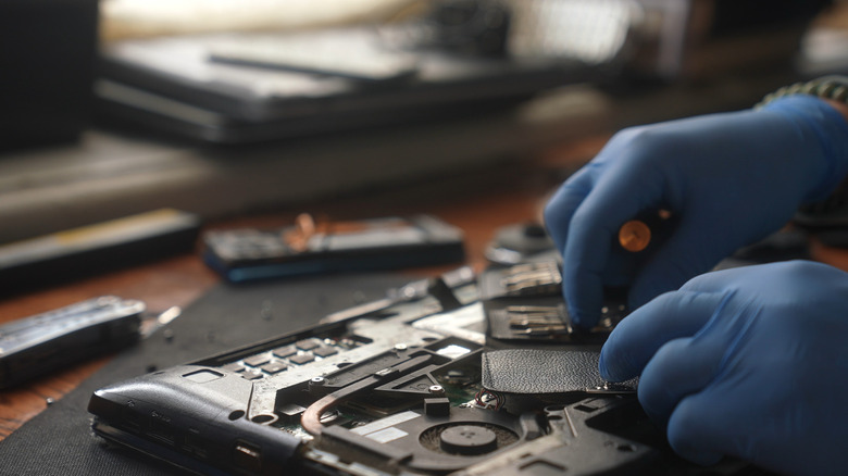 Person wearing blue gloves repairing a laptop using specialized tools