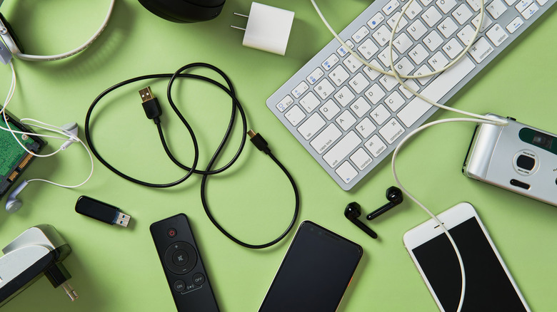 Used electronic devices including a keyboard, camera, smartphones, remote control, cables, flash drive, and adapter placed on a green surface
