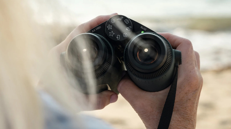 Hands holding Swarovski AX Visio 10x32 smart binoculars outdoors.