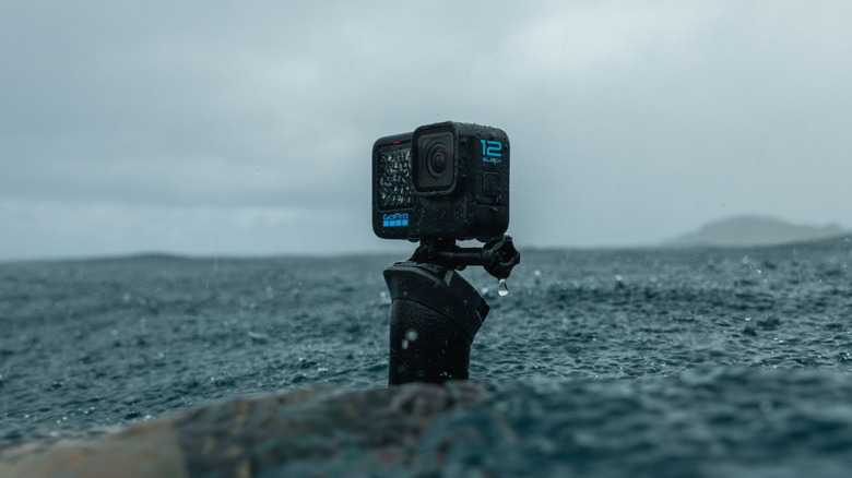 GoPro HERO12 Black action camera mounted on a handle in rough ocean water.