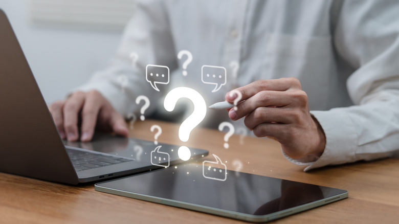 A person at desk pointing digital pencil at floating question and text notification boxes