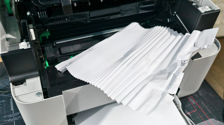 Stuck sheet of paper being removed from a printer with a full a paper tray