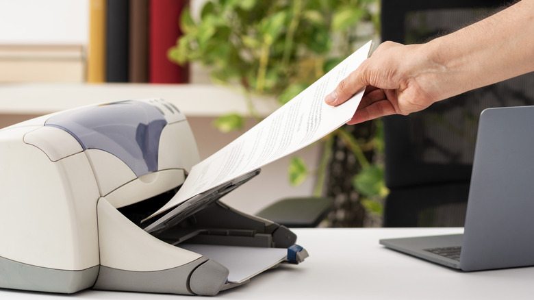 Person collecting a printed sheet from a white printer placed on a workstation