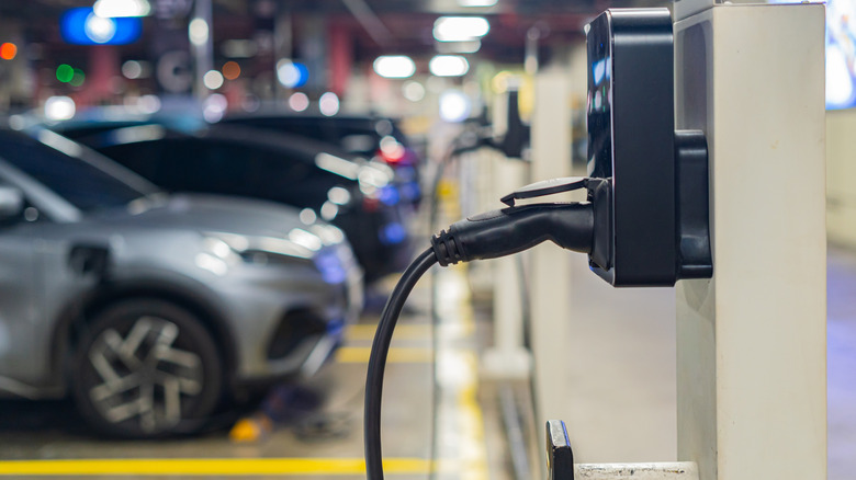 Electric vehicle charging station connector plugged in with EV parked in background