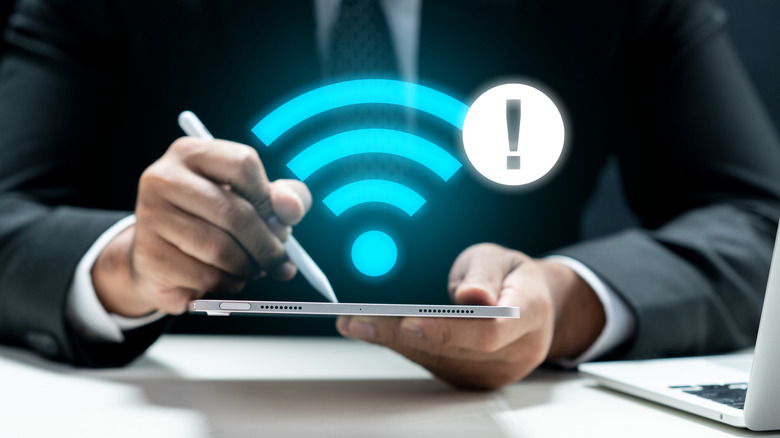 A person in a suit using a tablet with a Wi-Fi symbol and warning icon over it.