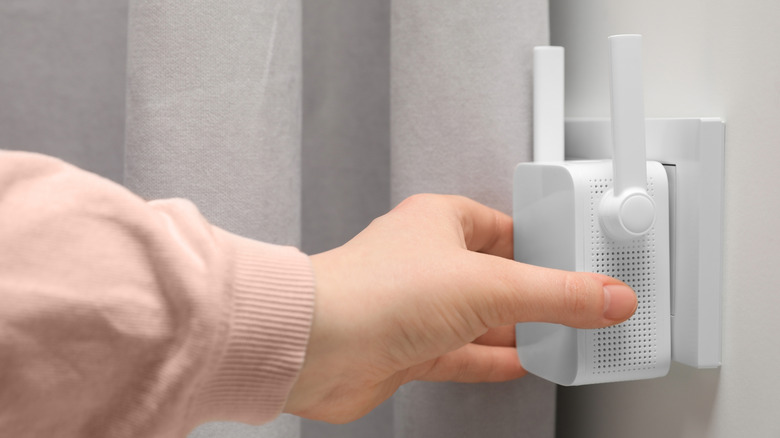 A person plugging a Wi-Fi signal extender into an outlet.