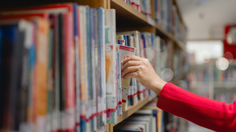 Person pulling a book from a library shelf.