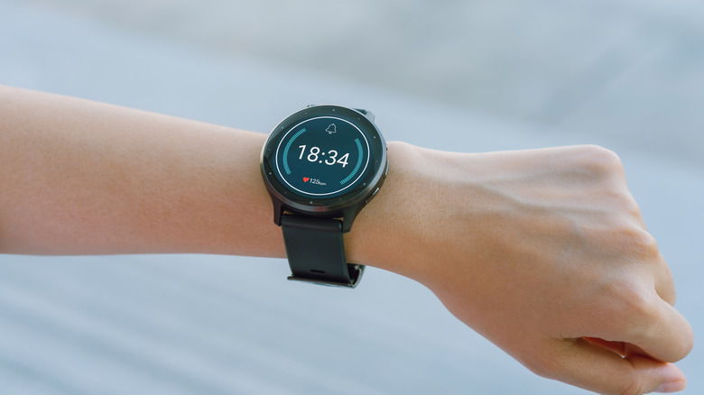 Smartwatch displaying time and heart rate on a person's wrist.