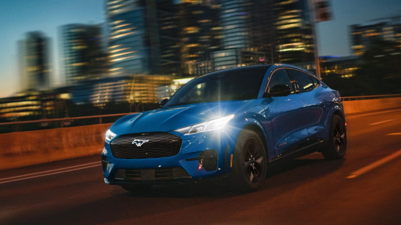 A blue Ford Mustang Mac-E GT driving through a city at night